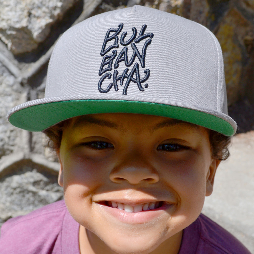 Boy wearing grey flat billed cap with Bulbancha embroidered in black thread.