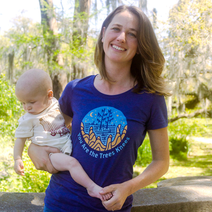Woman in trees knees shirt holding her infant with squeezebox onesie