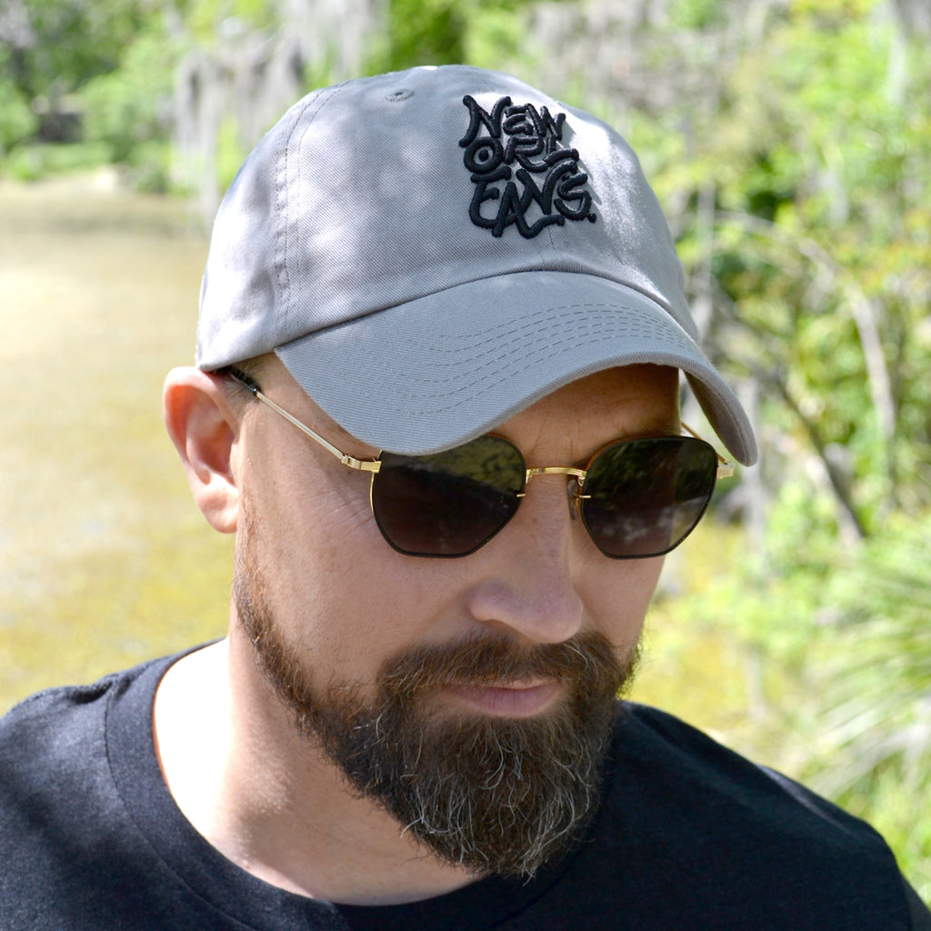 Man wearing grey curved brim cap with New Orleans embroidered in black thread.